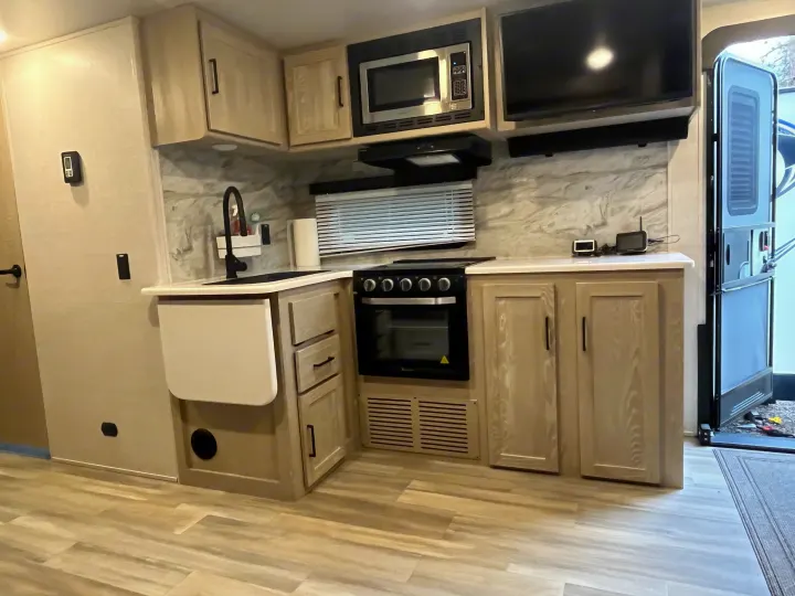 This RV rental's bright interior features a functional kitchenette: light wood cabinets, full oven, microwave, sink, & TV setup.. Forest River Rockwood Ultra Lite 2021