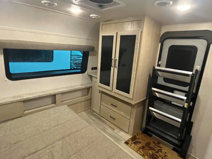 Experience comfort in this RV rental's bedroom, featuring a window, bed, light-toned cabinets, and sturdy entry steps.. Forest River Rockwood Ultra Lite 2021