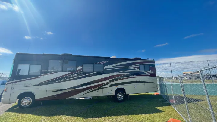 A large Georgetown Forest River RV rental parked on green grass under a sunny blue sky, alongside a metal fence.. Forest Rivers Georgetown 2013
