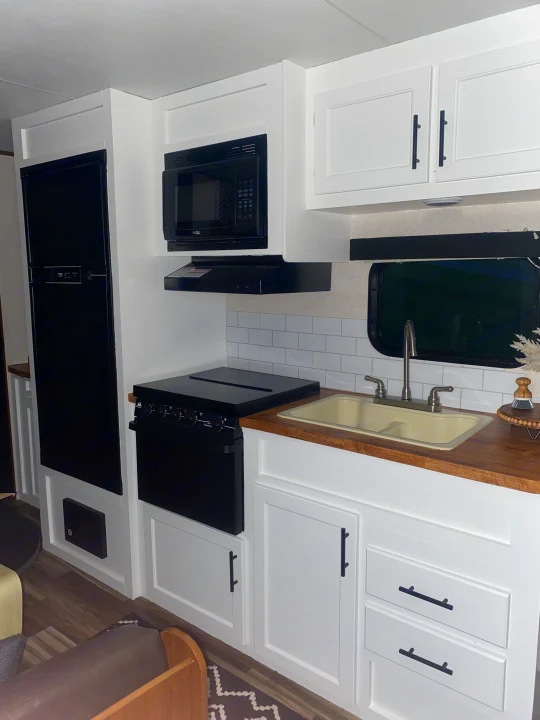 Bright RV rental kitchen interior: white cabinets, black appliances, wood counter, and subway tile backsplash.. Jayco Jay Flight 2017