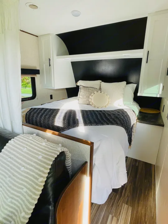 Bright RV rental bedroom: white bed with patterned throws, striking black accent wall, white cabinetry, and wood-look floor.. Jayco Jay Flight 2017
