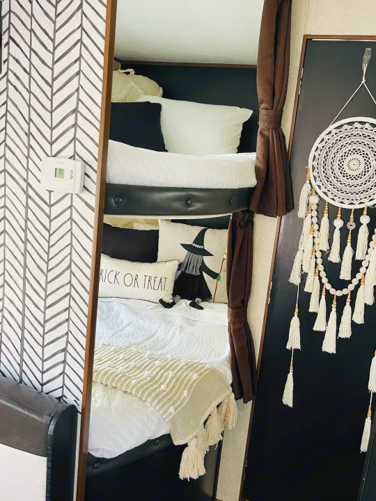 Inside an RV rental: black & white decor with patterned wallpaper, cozy bunk beds, witch pillow, & dreamcatcher.. Jayco Jay Flight 2017