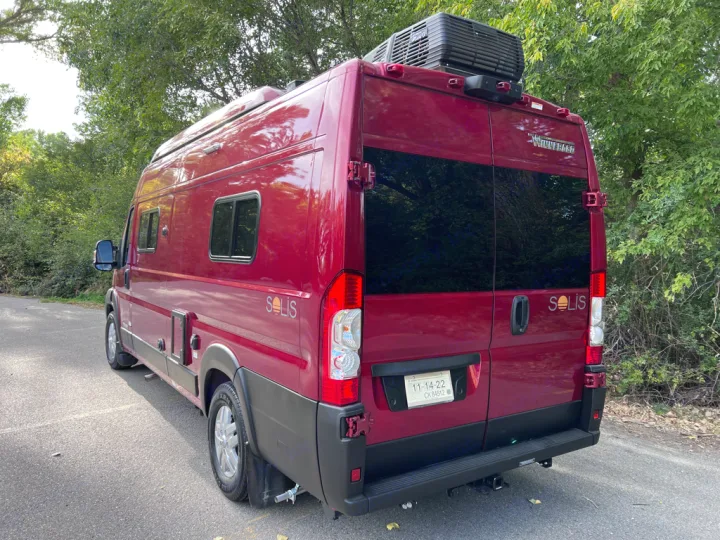 A sleek red Winnebago Solis camper van for rv rental, parked on a road with green trees. Perfect for adventure!. Winnebago Solis 59PX 2023