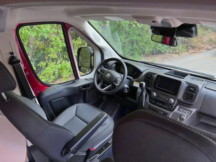 Inside this RV rental, see the modern front cabin with driver & passenger seats, dashboard, and steering wheel.. Winnebago Solis 59PX 2023