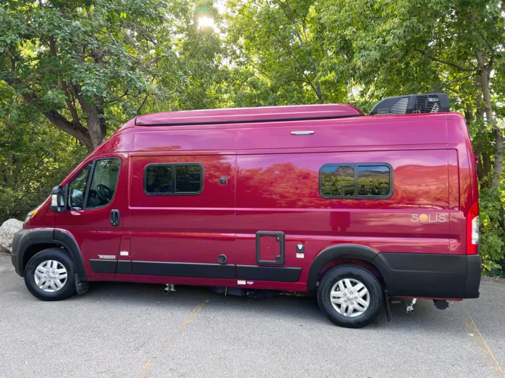 This maroon Winnebago Solis campervan is ready for your next rv rental adventure, parked among green trees.. Winnebago Solis 59PX 2023