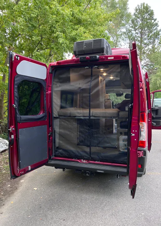 Open rear doors of a red camper van, revealing a bunk bed setup and insect screen, perfect for your next RV rental adventure.. Winnebago Solis 59PX 2023
