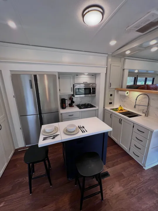 Explore this modern RV rental kitchen with stainless appliances, white cabinets, an island, and two dining stools.. Keystone RV Montana 2015