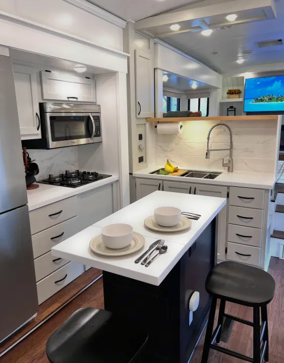 Bright and modern RV rental kitchen featuring white cabinets, stainless steel appliances, and a dining island.. Keystone RV Montana 2015