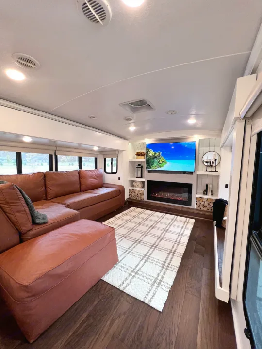 Spacious RV rental interior featuring a modern living room with a large brown sectional, fireplace, TV, and wood-look floors.. Keystone RV Montana 2015