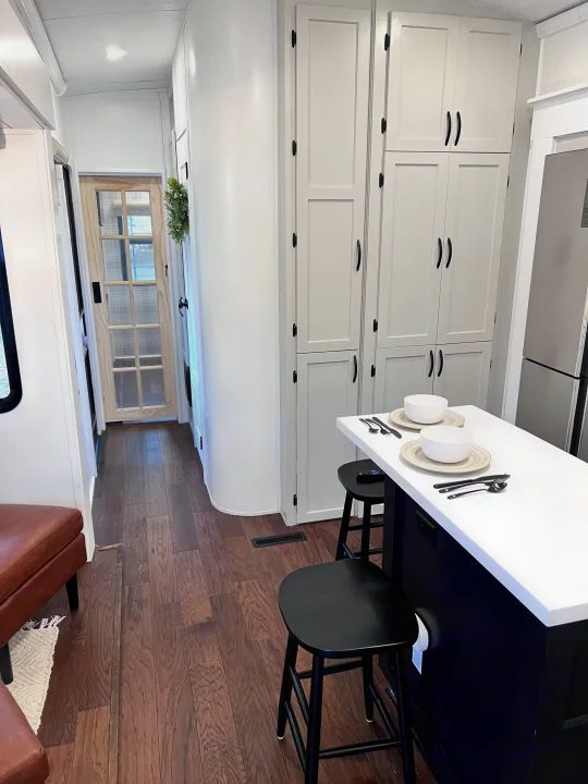 RV rental kitchen interior: white cabinets, island, black stools, wood floors, and a hallway with a door.. Keystone RV Montana 2015