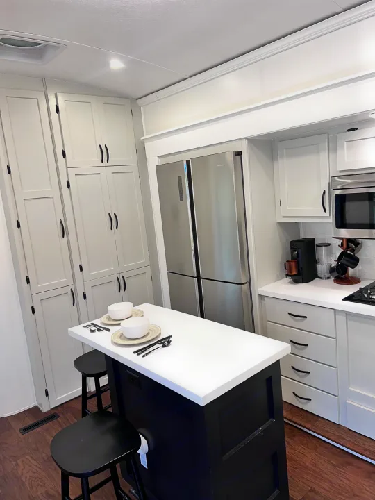 Modern RV rental kitchen showcasing light gray cabinets, a Hisense fridge, and a black island with white top, set for two.. Keystone RV Montana 2015