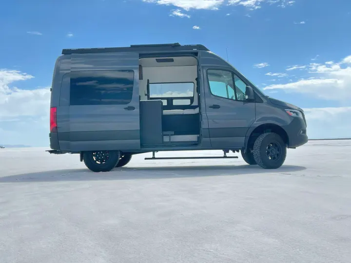 Explore in this dark grey Sprinter camper van RV rental, parked on salt flats with its side door open, ready for adventure.. Mercedes-Benz Sprinter 2021