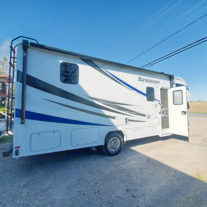 This white Sunseeker RV rental, with an open door, is parked on gravel under a clear blue sky, ready for travel.. Forest River Sunseeker 2020