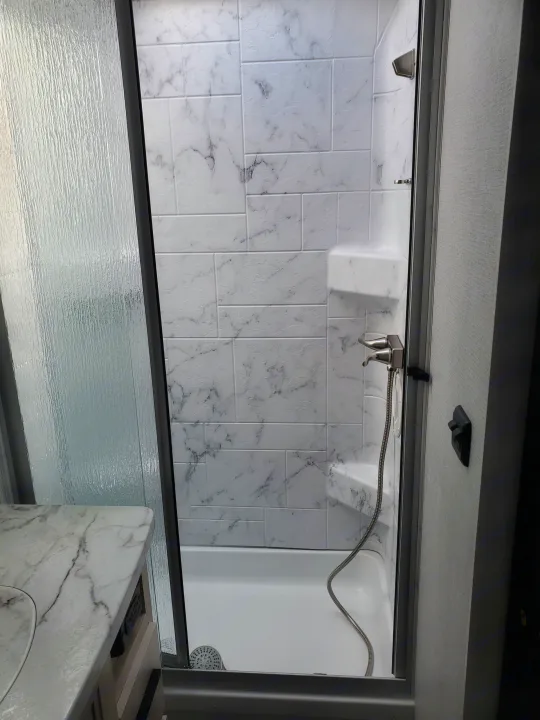 RV rental bathroom: Modern shower with textured glass door, faux marble walls, and a built-in seat.. Forest River Sunseeker 2020