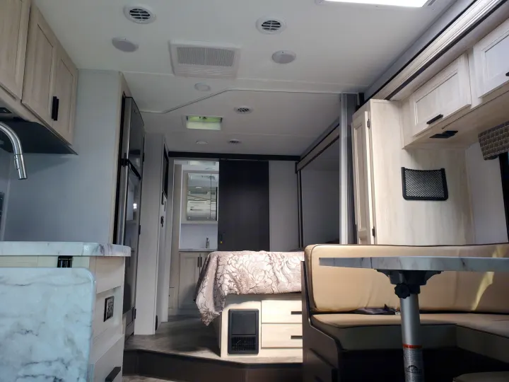 Inside a modern rv rental, showing a well-lit kitchen, dining area, and bedroom, offering a comfortable living space on the road.. Forest River Sunseeker 2020