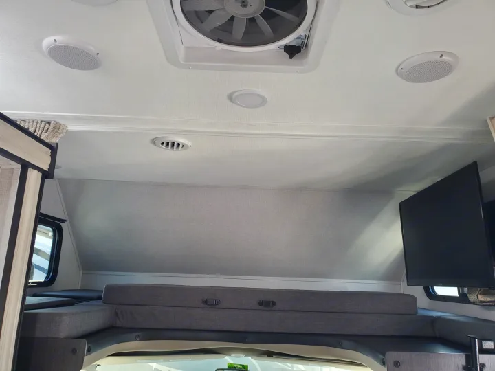 Cozy RV rental interior: view of overhead bunk with gray cushions, wall-mounted TV, ceiling fan, air vent, and speakers.. Forest River Sunseeker 2020