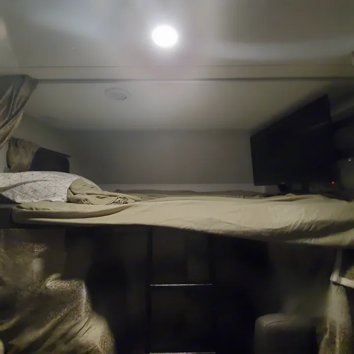 Cozy RV rental bunk bed area with soft bedding, a wall-mounted TV, and bright overhead light. Ideal for travel.. Forest River Sunseeker 2020