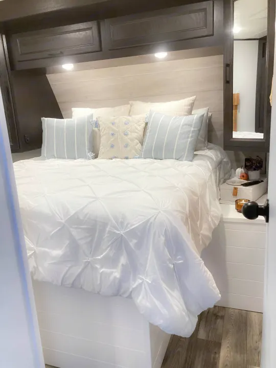 Cozy modern RV rental bedroom with white bedding, blue pillows, and storage. Perfect for comfortable travel.. Jayco Eagle HT 2022