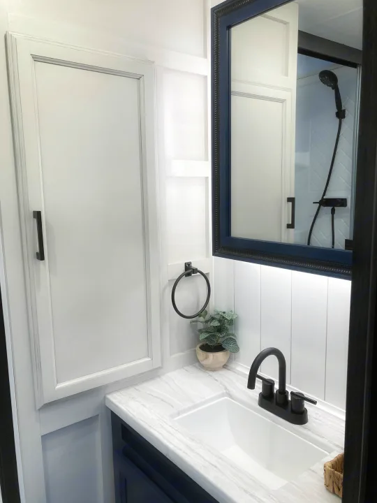 Modern RV rental bathroom with white cabinetry, marbled counter, black faucet, and a mirror reflecting the shower.. Jayco Eagle HT 2022