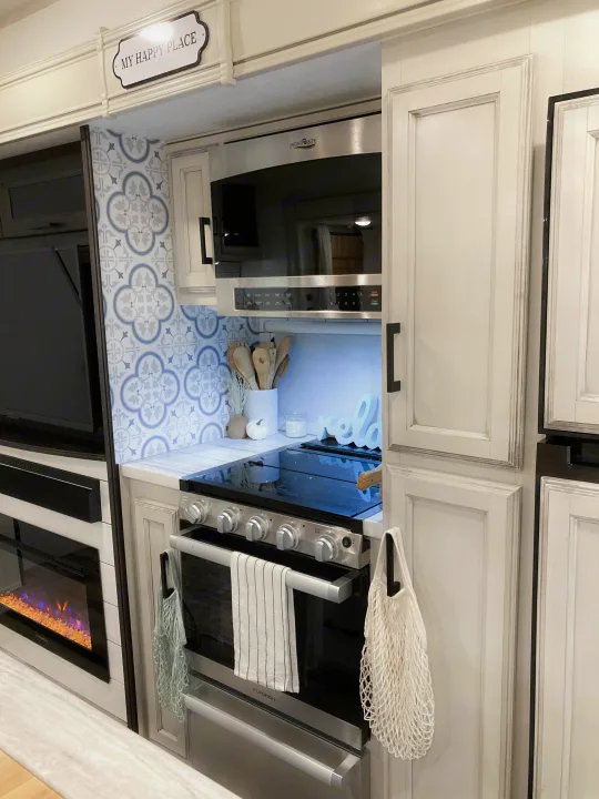 Modern RV rental kitchen: blue tile backsplash, microwave, stove, and fireplace. Your happy place on wheels.. Jayco Eagle HT 2022