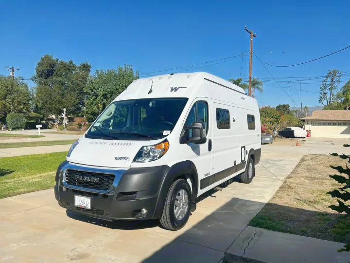 White Winnebago Ram ProMaster camper van for RV rental, parked on a driveway on a sunny day.. Winnebago Solis 2023