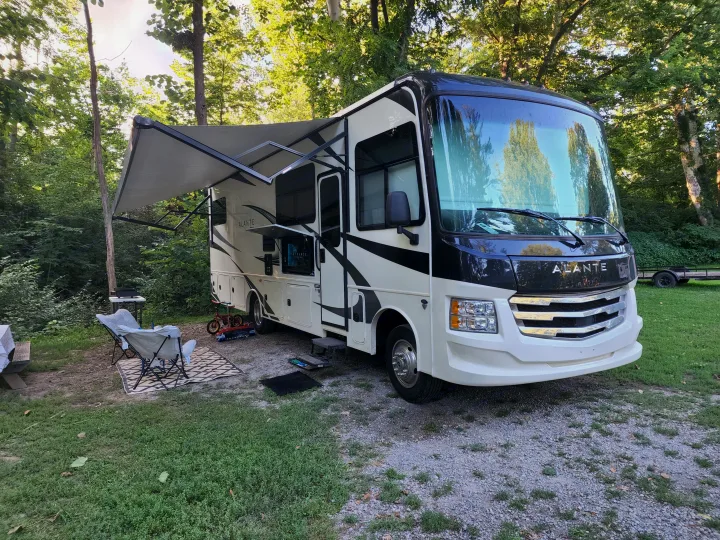 An rv rental at a leafy campsite, featuring an extended awning, outdoor TV, chairs, and grill setup for a cozy stay.. Jayco Alante 2022