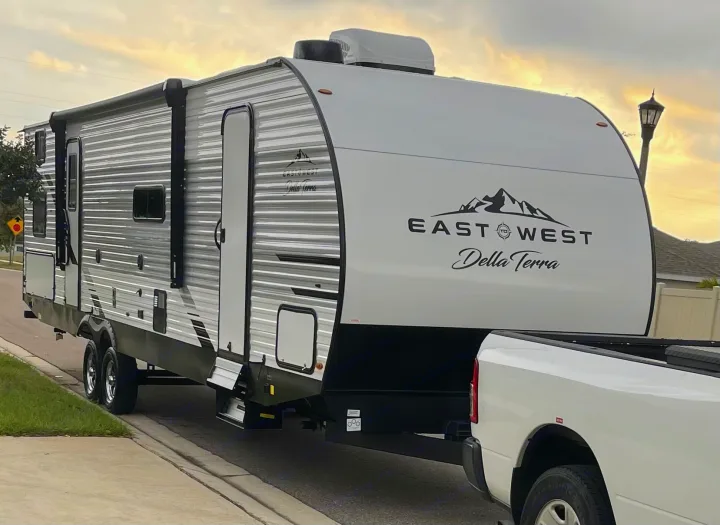 A white and gray East West Della Terra travel trailer, perfect for an rv rental, hitched to a pickup truck, ready for camping adventures.. Della Terra 312H Della Terra 2023