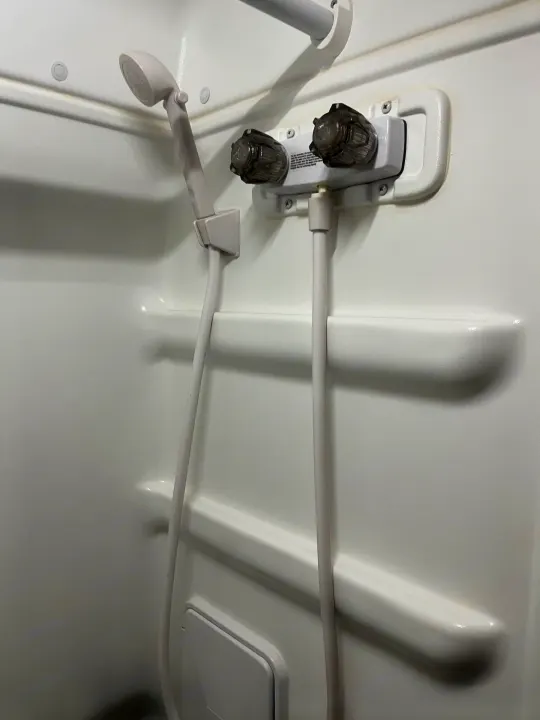Interior of a compact white RV rental shower with handheld shower head, hot/cold faucet, and integrated shelving.. Winnebago Solis 2021