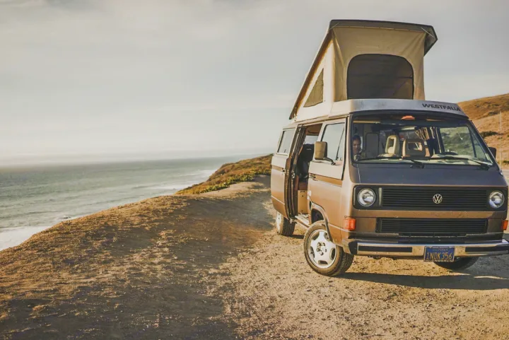 Coastal RV rental dream: Brown Westfalia camper van with pop-top open on a dirt road overlooking the vast ocean.. Volkswagen Vanagon 1985