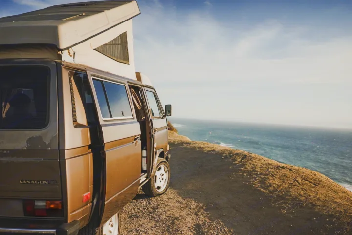 Brown VW Vanagon pop-top camper van on a coastal cliff overlooking the ocean. Perfect RV rental for your next adventure!. Volkswagen Vanagon 1985