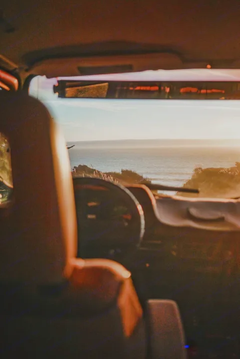 View from an RV rental dashboard showing a sunlit ocean and coastline. Interior seat on left, perfect for a scenic road trip.. Volkswagen Vanagon 1985