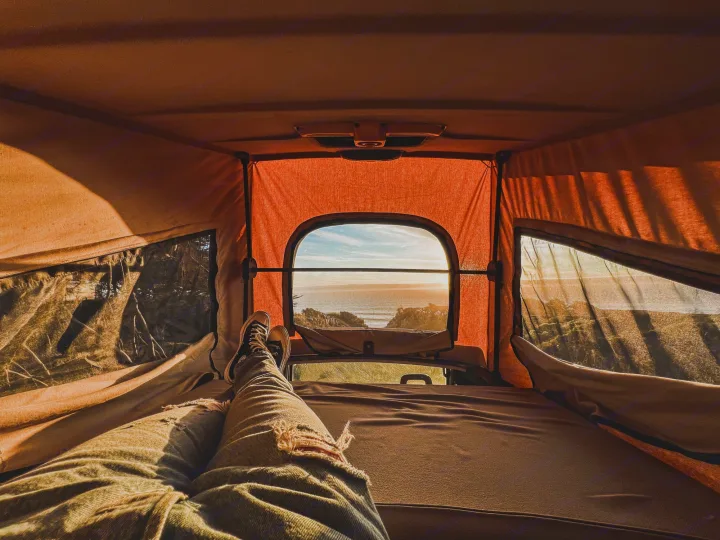 POV from an RV rental bed: legs stretched out, watching a golden ocean sunset from inside a pop-up camper.. Volkswagen Vanagon 1985