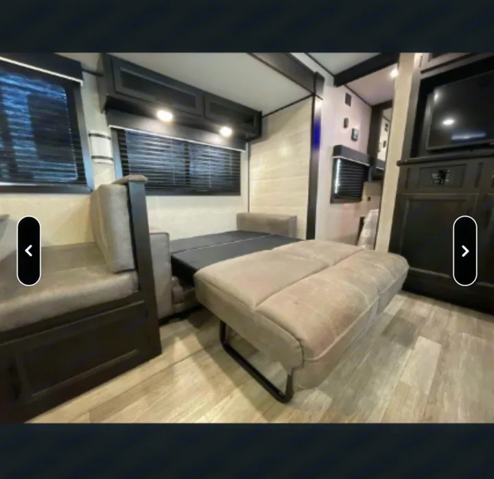 Inside an RV rental: a light-colored, pull-out sofa converts to a bed, with storage cabinets, windows, and a TV setup.. Jayco Jay Flight SLX Rocky Mountain Edition 2022