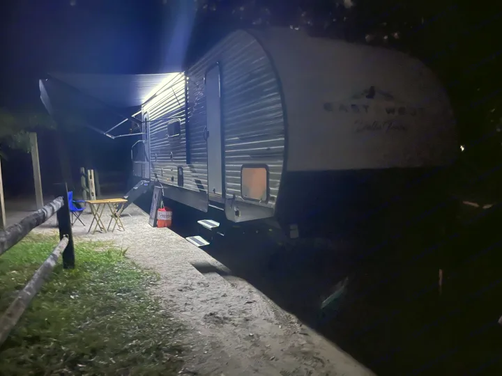 This cozy RV rental travel trailer is lit up at night, showcasing its illuminated awning and outdoor seating area for comfortable camping.. Della Terra 312H Della Terra 2023