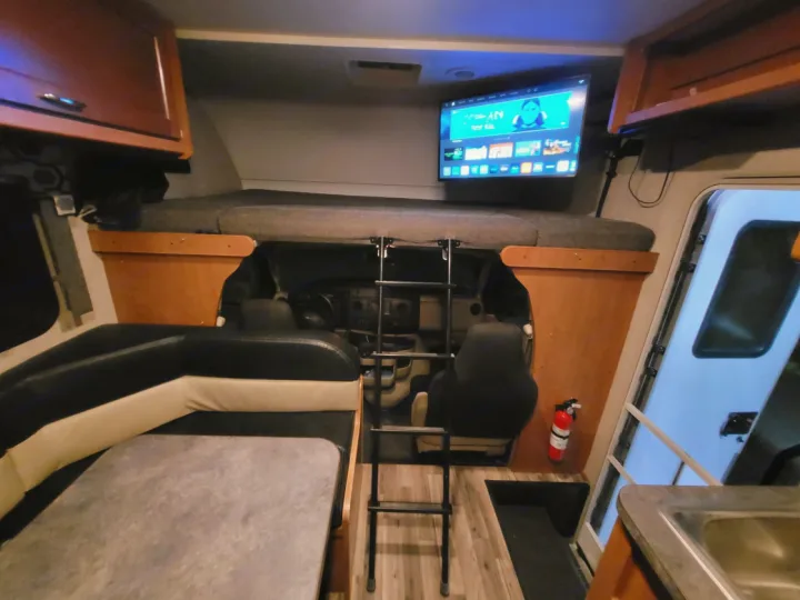 An RV rental's interior, showing a front bunk bed with ladder, mounted TV, dining area, and driver's cabin.. Winnebago Minnie Winnie 2018