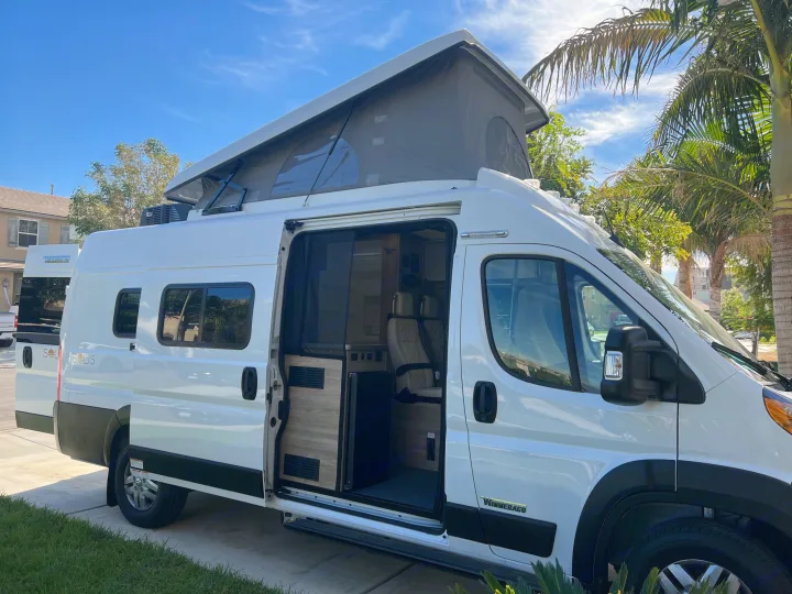 White Winnebago Solis RV rental van with pop-top extended and interior visible through open side door.. Winnebago Solis 2023