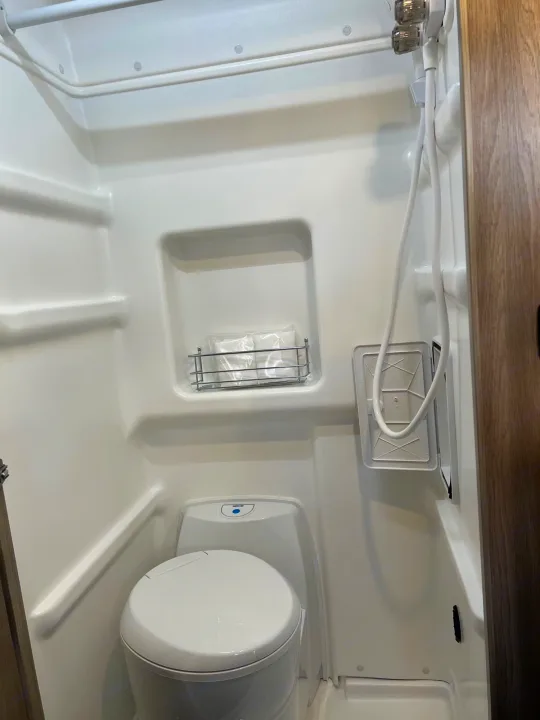 Inside an RV rental: a compact white wet bath with toilet, wall-mounted shower, and built-in storage.. Winnebago Solis 2023
