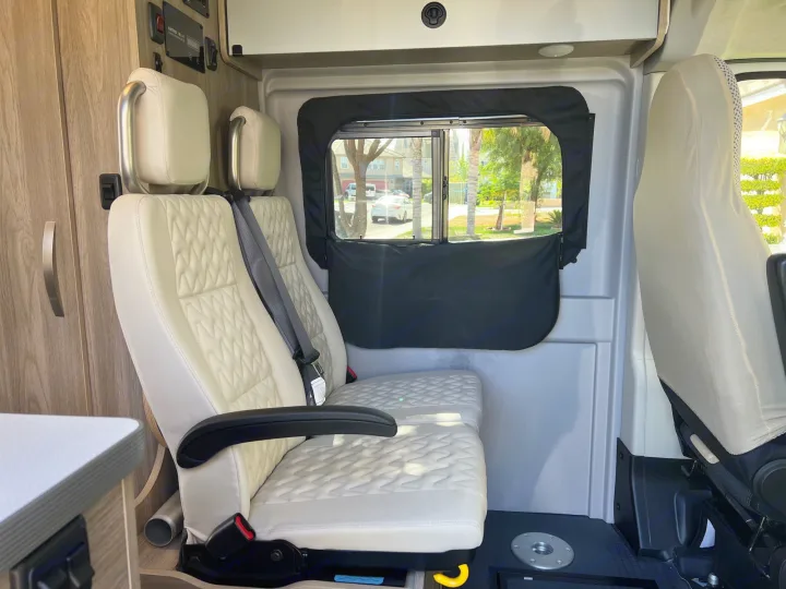 Explore this RV rental's cozy interior: passenger seats, window, control panel, and wood accents. Ready for your trip!. Winnebago Solis 2023