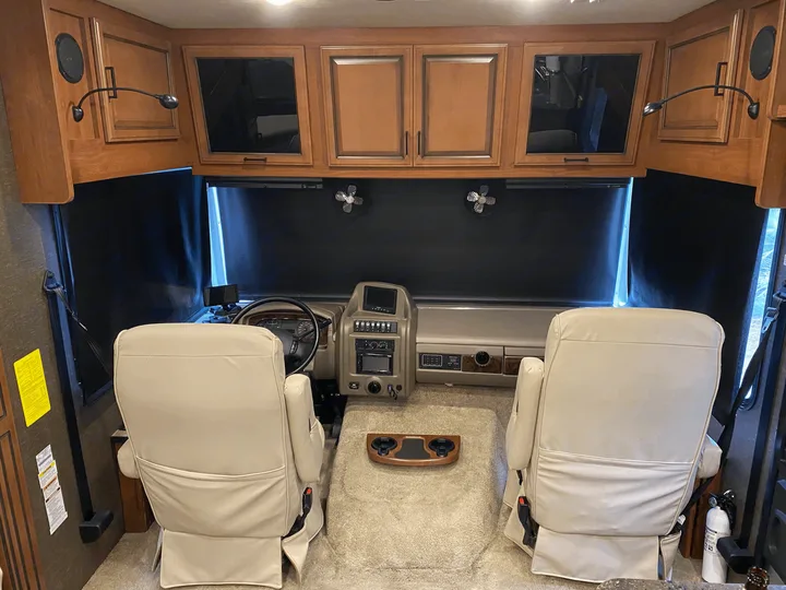 Inside a comfortable RV rental: the front cockpit with cream seats, dashboard, and overhead storage for easy travel.. Fleetwood Bounder 33C 2014