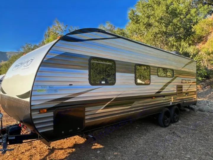 Sleek travel trailer RV rental parked at a scenic campsite. Features a striking striped design and large windows for outdoor views.. Forest River EVO Select 268 BH 2022