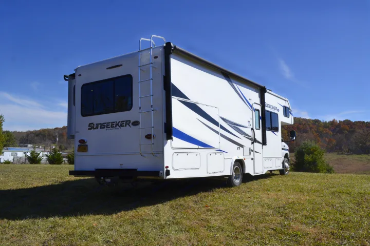 A pristine white Sunseeker RV rental, equipped with a ladder and awning, awaits its next journey on a sunny field.. Forest River Sunseeker Classic 2021