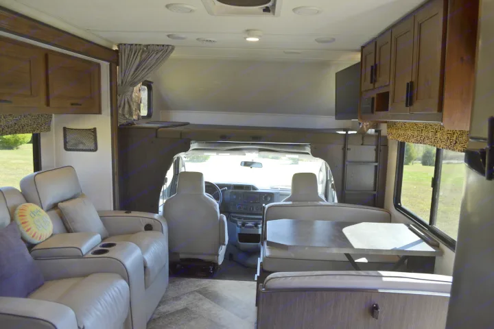 Inside a comfortable RV rental: living area with recliners, convertible dinette, driver's cockpit, and overhead bunk.. Forest River Sunseeker Classic 2021