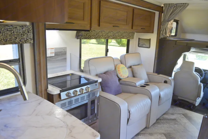 RV rental interior: A bright living area with light-colored recliners, full kitchen (stovetop, microwave), and cabinets.. Forest River Sunseeker Classic 2021