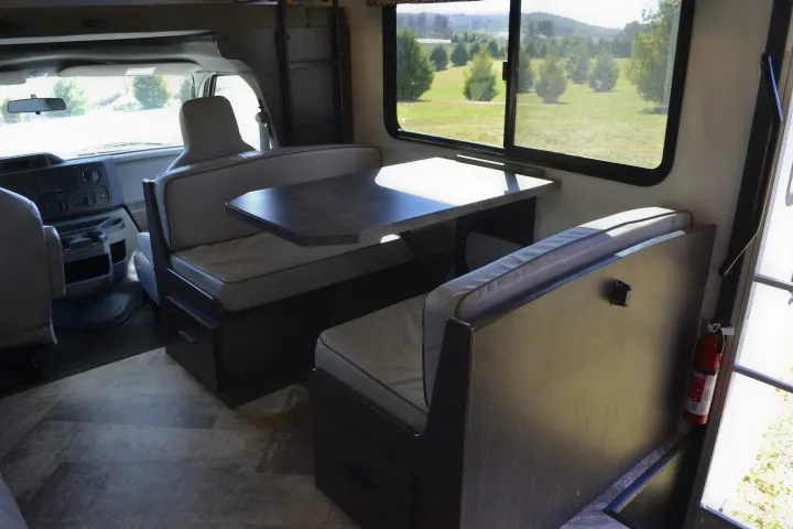 Inside an RV rental: a cozy dinette with window view, driver's area, and safety features like a fire extinguisher.. Forest River Sunseeker Classic 2021