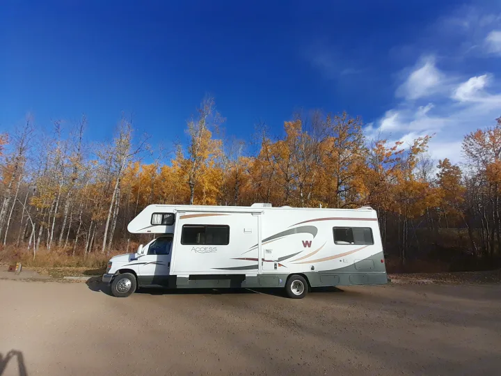 A white RV is parked among vibrant autumn trees under a bright blue sky, ideal for an RV rental adventure.. Winnebago Access 2008