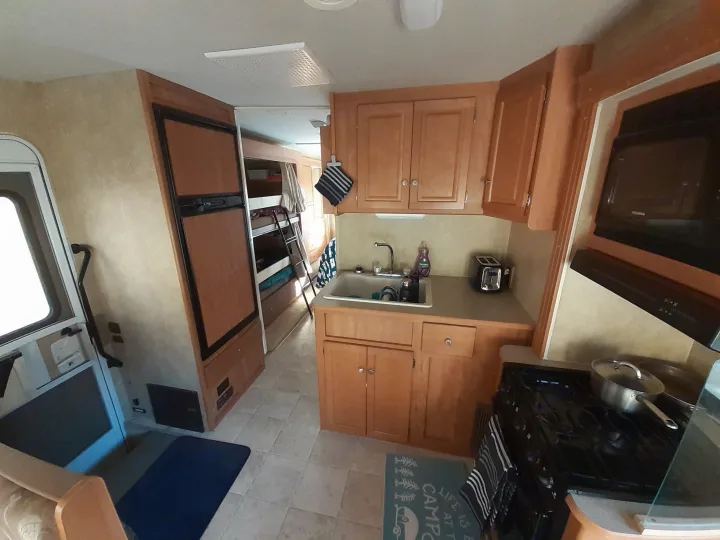 Inside an RV rental: kitchen with sink, stove, microwave, fridge, and adjacent bunk beds for travel comfort.. Winnebago Access 2008