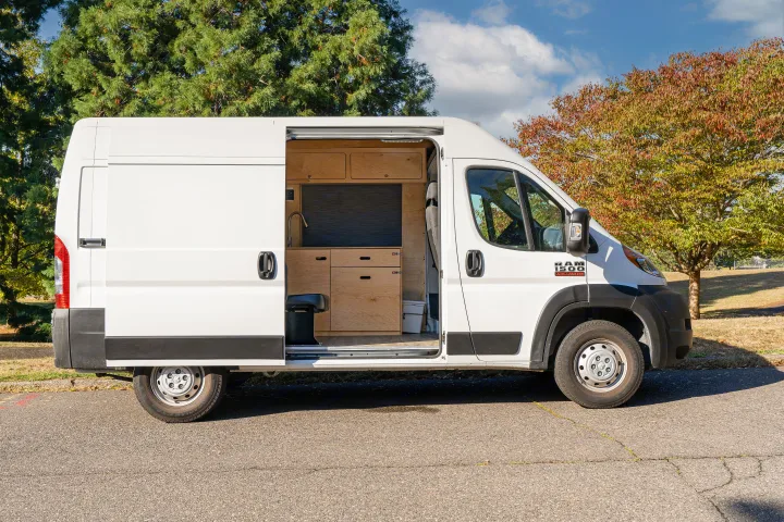 White Ram ProMaster RV rental with open side door revealing custom wood interior, parked outdoors.. RAM ProMaster 2022