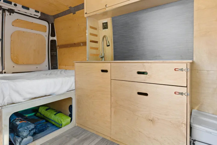 Spacious RV rental interior with a cozy bed, ample under-bed storage, and a compact kitchen area with sink and cabinets.. RAM ProMaster 2022