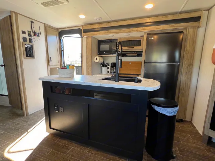 Spacious modern RV kitchen with a central island, black appliances, and control panel, ideal for your next RV rental adventure.. Forest River Cherokee Alpha Wolf 2021