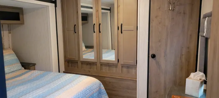 Inside an RV rental: a compact bedroom features a striped bed, mirrored wardrobe, and practical storage solutions.. Palomino RBFQ 2022